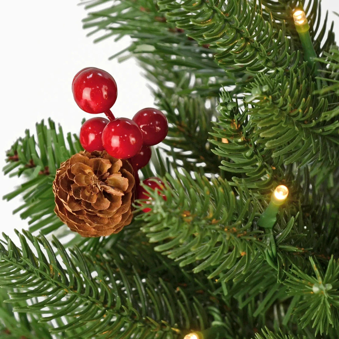 Close up of red berries and pine cone on a green pine Christmas tree with warm white fairy lights