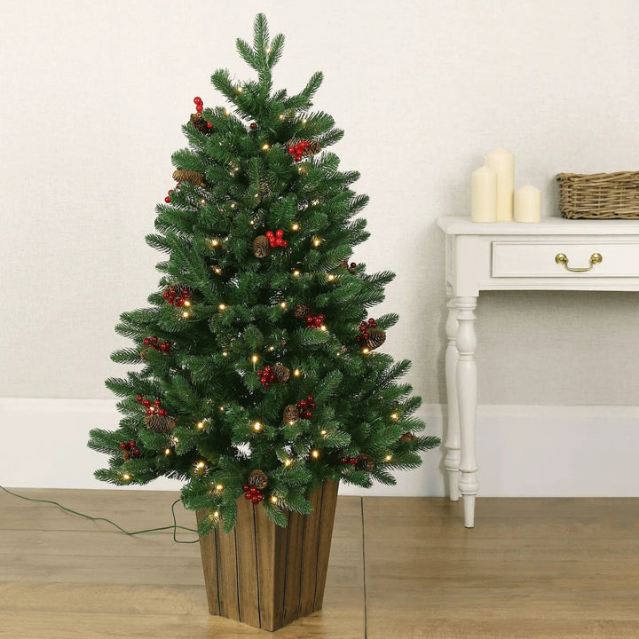 Small green Christmas tree lit up with fairy lights and decorated with pine cones and red berries