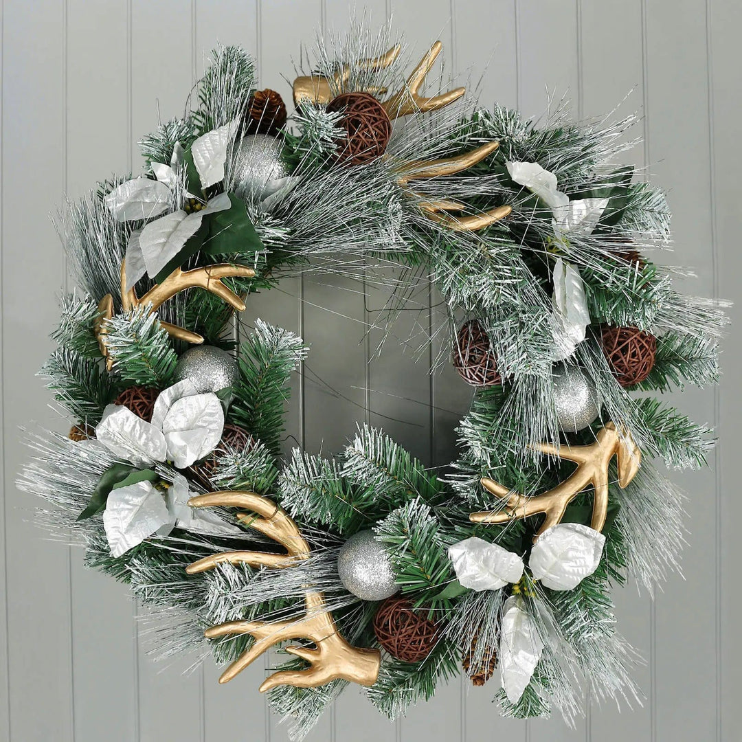 Silver and gold Christmas wreath with reindeer antlers, frosted pine branches, poinsetties and glitter baubles on a wood panelled wall