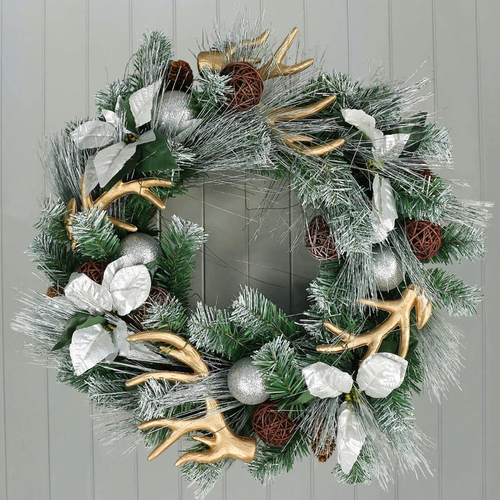 Silver and gold Christmas wreath with reindeer antlers, frosted pine branches, poinsetties and glitter baubles on a wood panelled wall