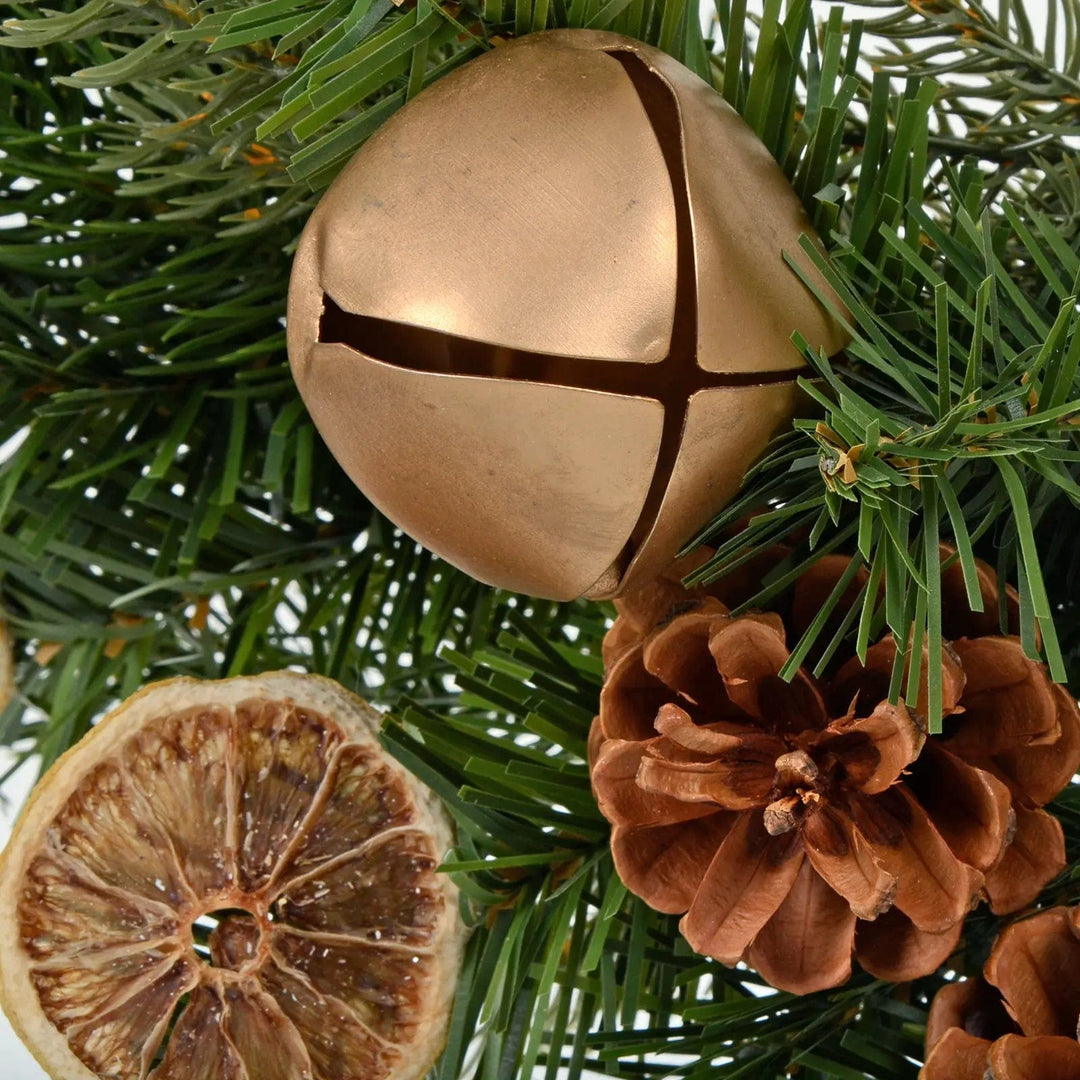 Close up of gold sleigh bell, pine cone and dried orange slice on green pine Christmas wreath