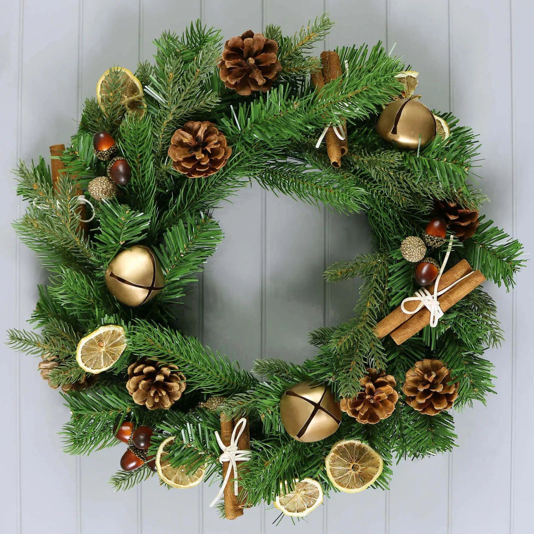 Green and gold Christmas wreath with bells, cinnamon, cones and acorns on a wood panelled wall