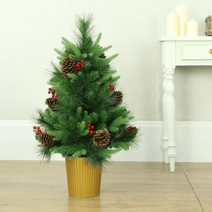 Small green pine Christmas tree with cones and berries, in a gold pot on a hardwood floor