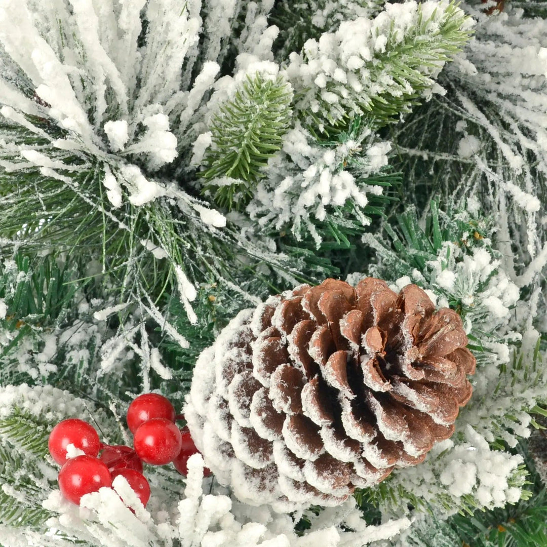 Close up of a pine cone and red berries on a snow covered artificial Christmas tree