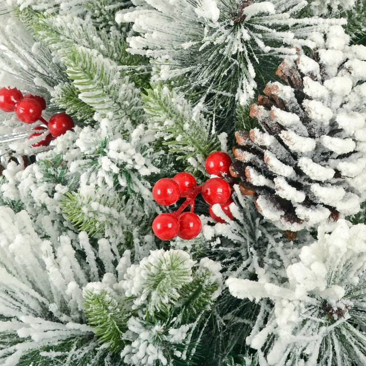 Close up of a snow covered pine cone and red berries on a green pine Christmas tree