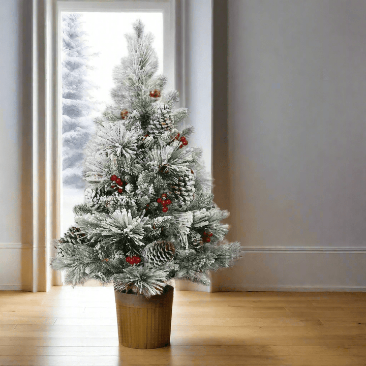 Artificial snow covered Christmas tree with pine cones, red berries in a gold coloured pot