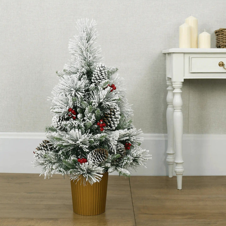 Small snow covered Christmas tree decorated with pine cones and berries in a gold pot on hardwood flooring