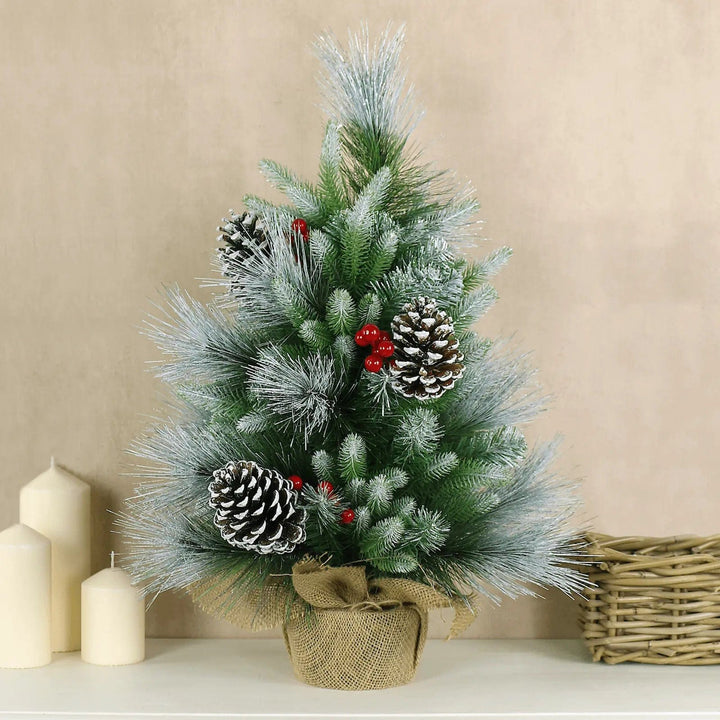 Small frosted Christmas tree with cones and berries on a table with ivory church candles