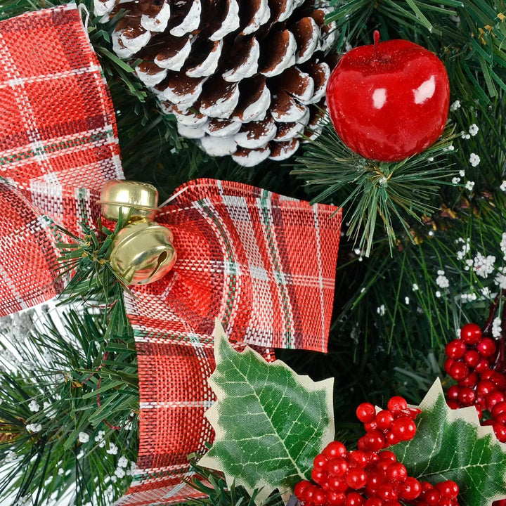 Close up of gold bells, red tartan bow, pine cone, holly berries and red apple on a snow covered Christmas tree