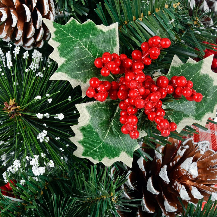 Holly leaves with a bunch of red berries on a snow flocked Christmas tree