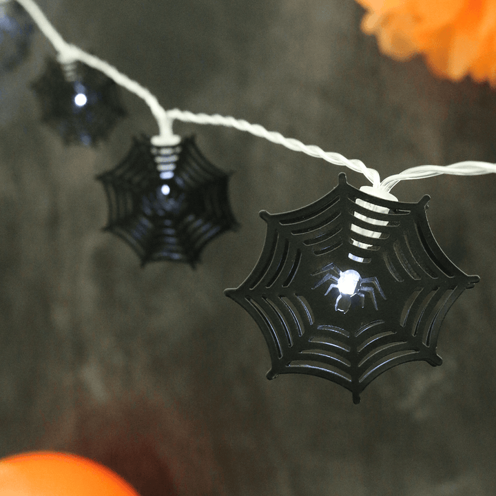 black metal spider web halloween lights on transparent string on black background with orange decorations in the background