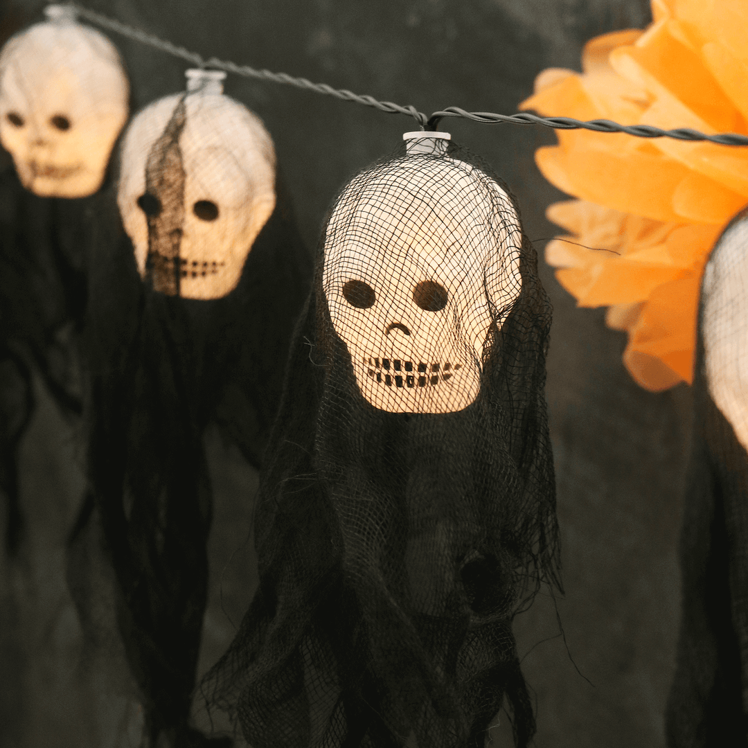 3 demon skull string lights featuring warm white led light with black cloche material on black background with orange decorations in the background