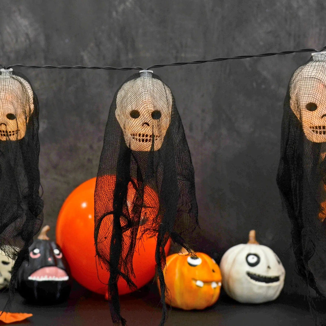 Halloween skull string lights with black fabric shrouds over a table with pumpkins and orange balloons