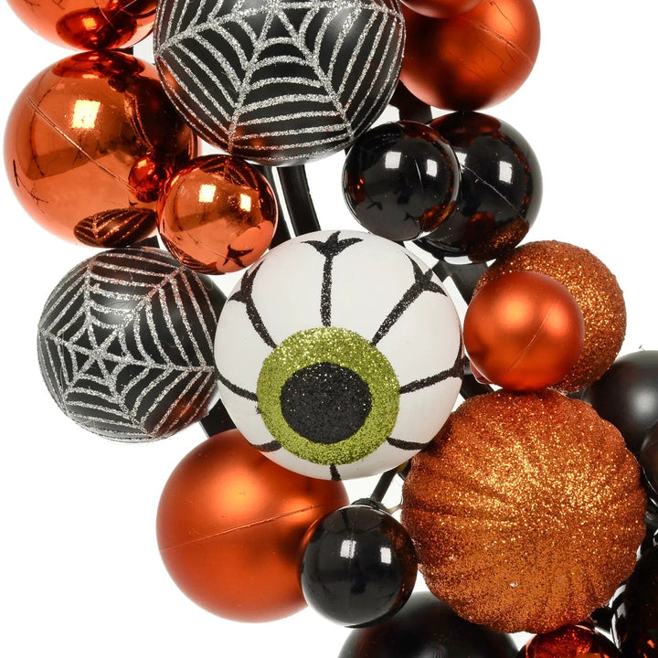 Green eyeball, orange glitter pumpkin, spider web, black and orange baubles on a Halloween wreath