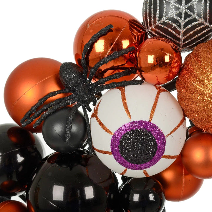 Black glitter spider, purple eyeball, black and orange baubles on a Halloween door wreath