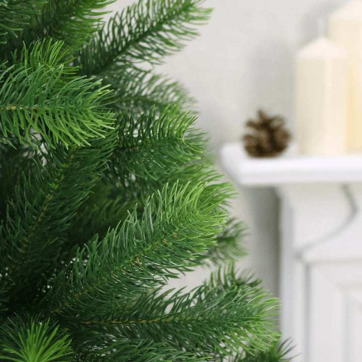 Close up of green plastic branches on pine Christmas tree with fireplace in the background