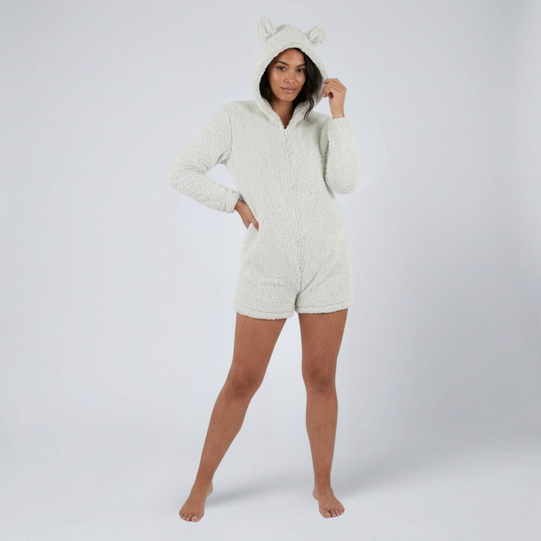 A woman modeling a cream-colored, textured sherpa hooded romper with bear ears on the hood, photographed against a light gray studio background.