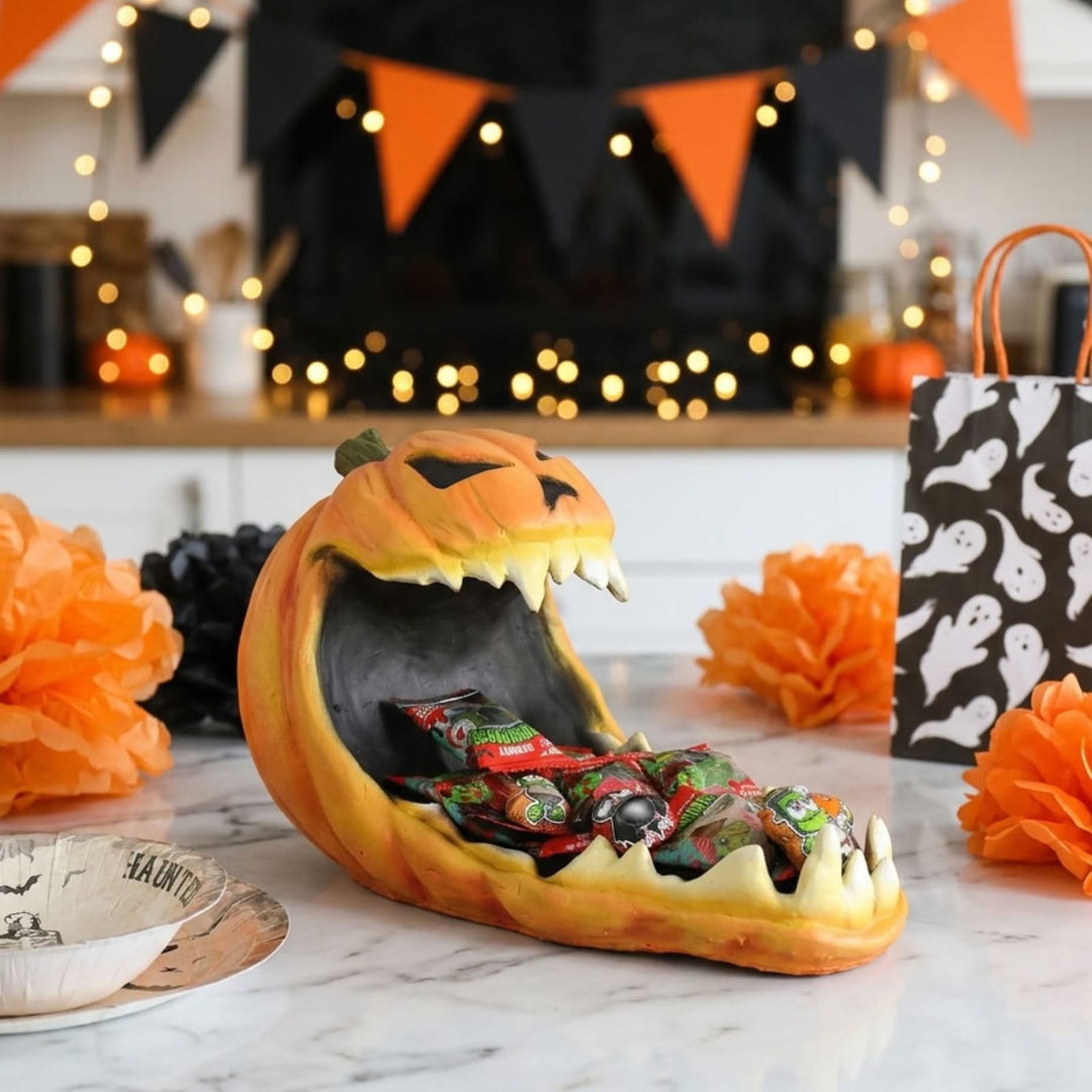 pumpkin candy holder on kitchen counter with halloween decorations and lights in background