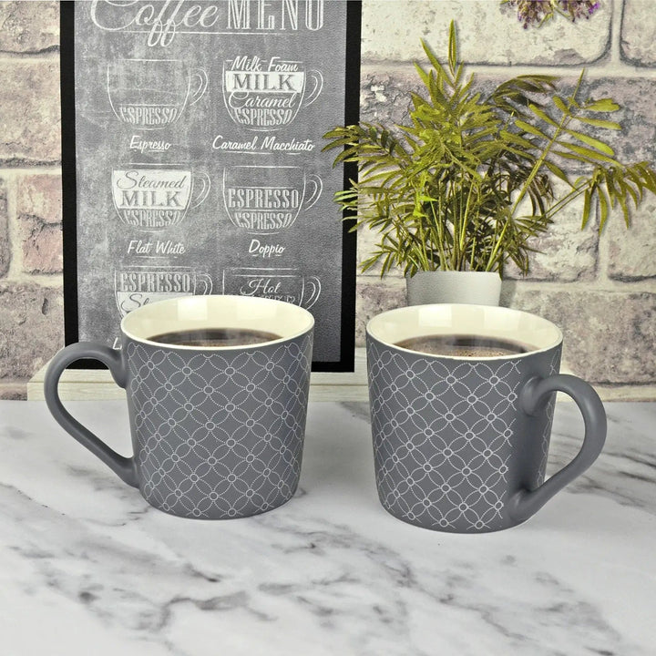 2 mugs of coffee with dark grey and silver circular pattern on a marble kitchen worktop with cafe wallpaper