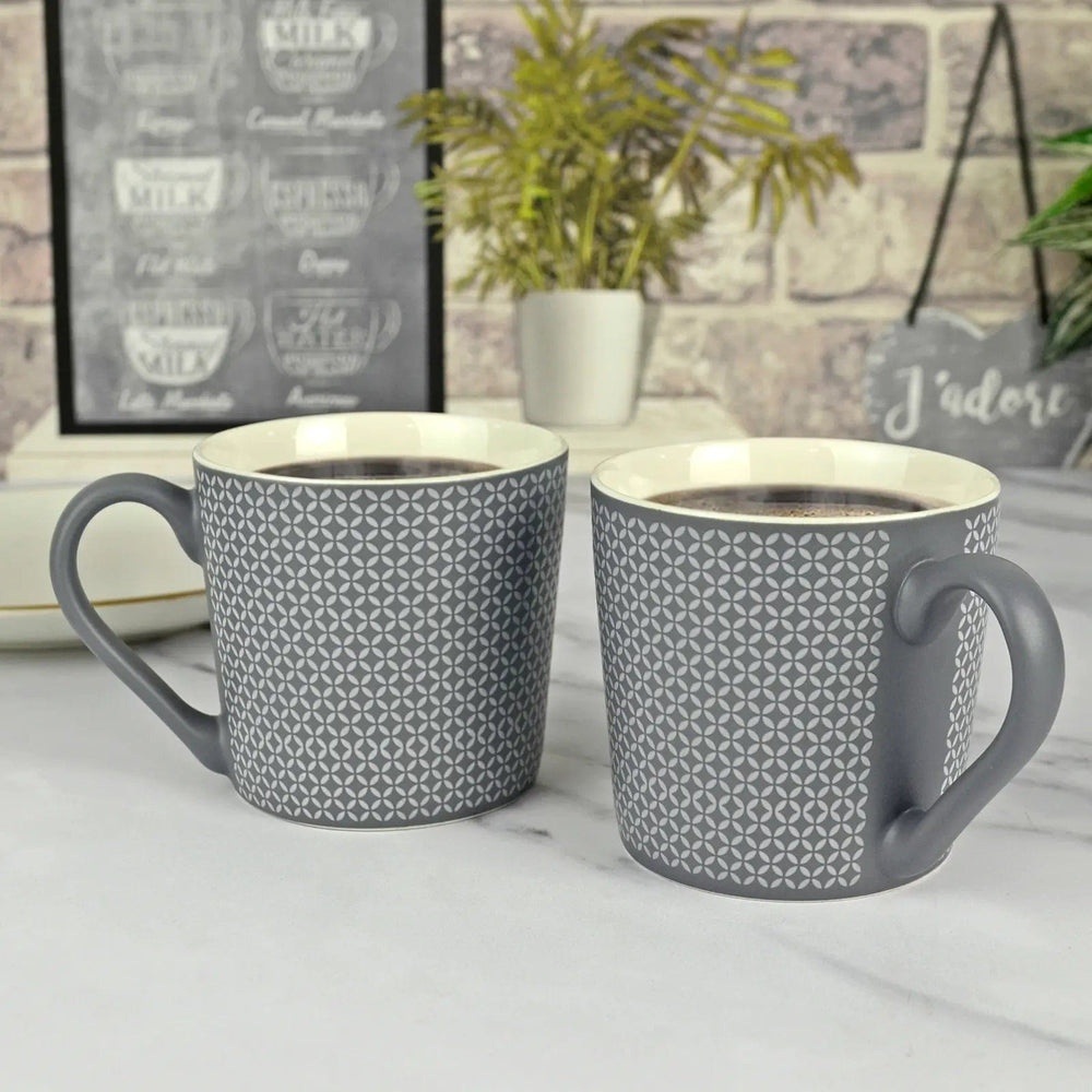 2 grey patterned coffee mugs on a marble worktop with plants