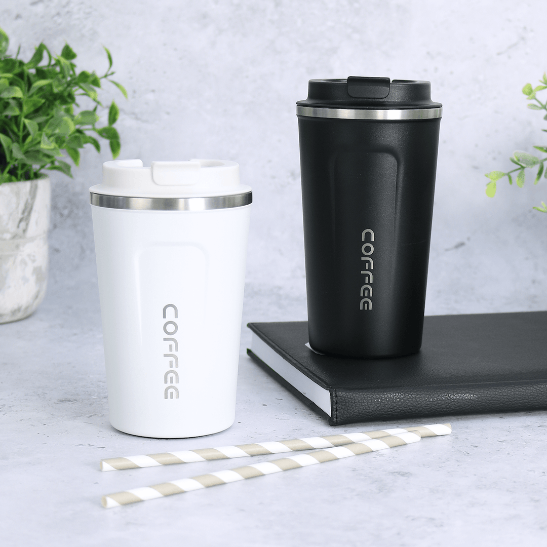 black and white coffee mugs in different sizes sitting on top of black book on concrete background with grey striped straws in the foreground