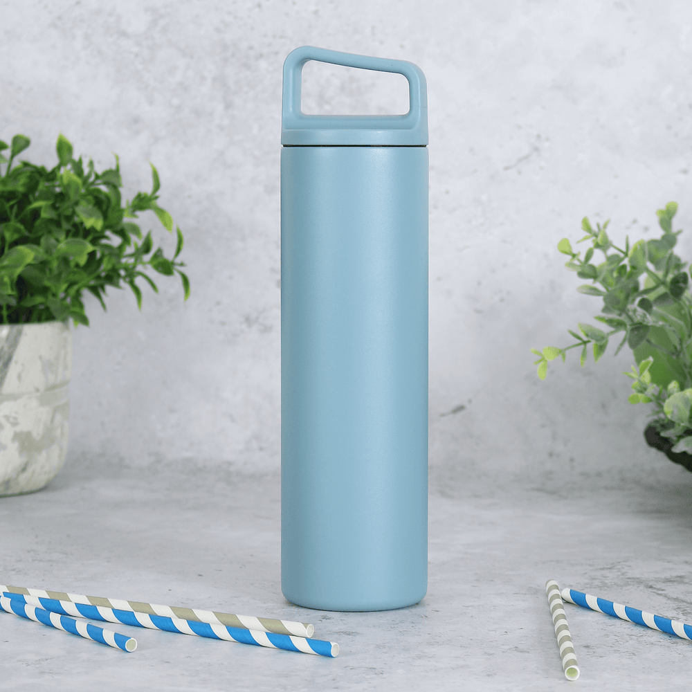 blue stainless steel water bottle with carry handle lid on concrete surface with plants in the background and grey and blue striped straws in the foreground