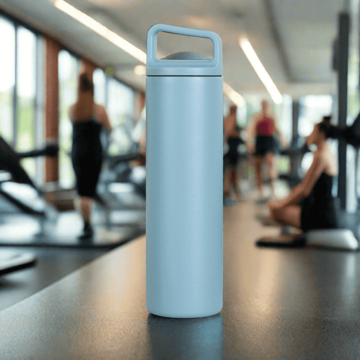 blue stainless steel water bottle with carry handle lid on tabletop surface with a Gym in the background.