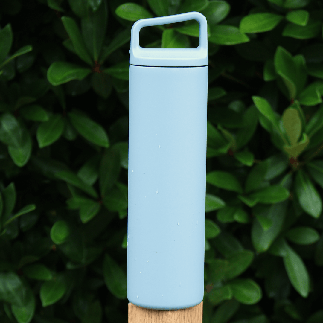 blue stainless steel water bottle on fence post with evergreen tree in the background outdoors