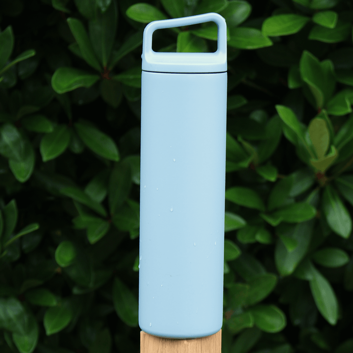 blue stainless steel water bottle on fence post with evergreen tree in the background outdoors