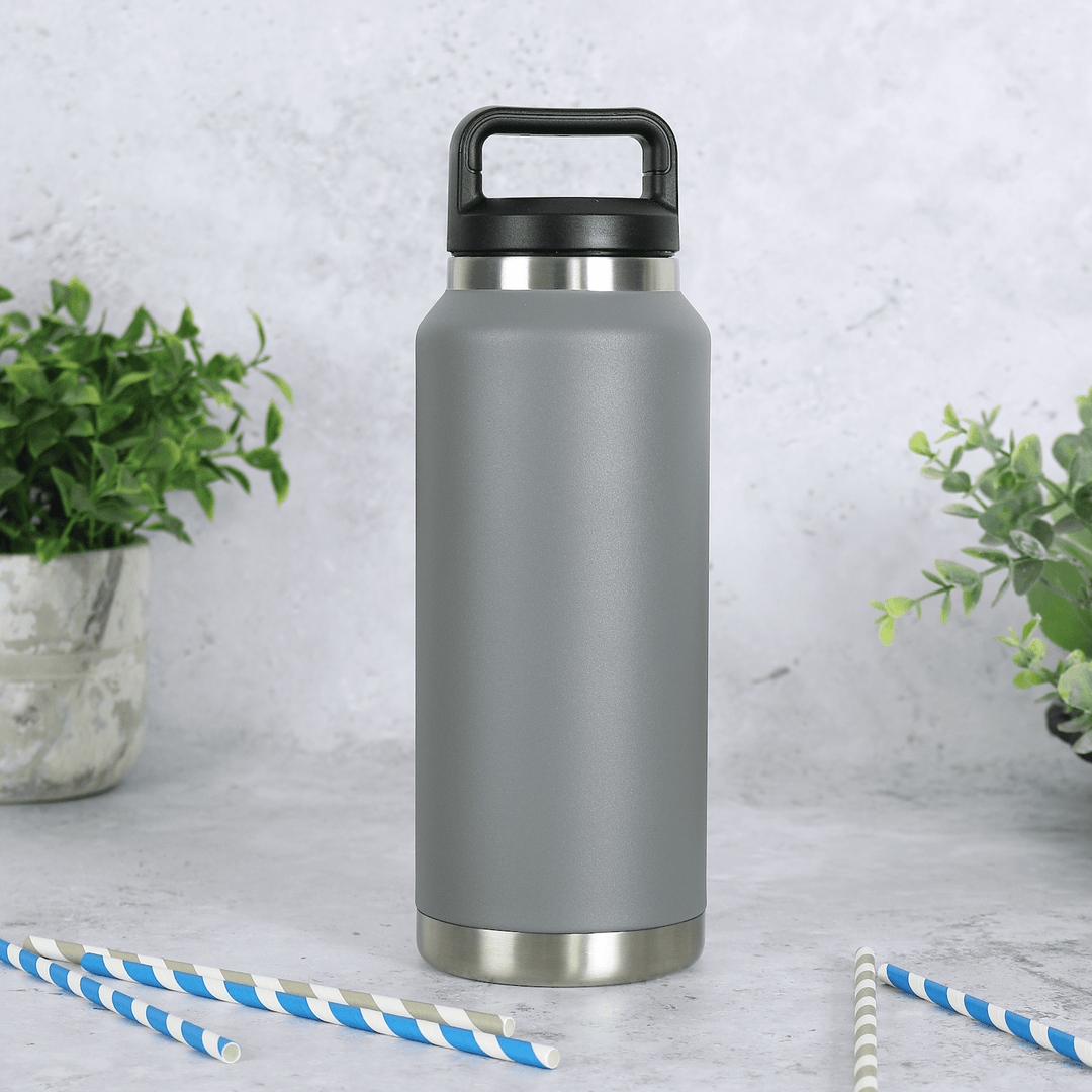 large grey heavy duty stainless steel water bottle on concrete surface with plants in the background and blue and grey striped straws to in the foreground