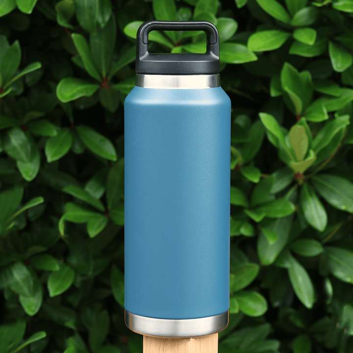 large blue heavy duty water bottle with carry handle lid on fence post in front of ever green tree outdoors