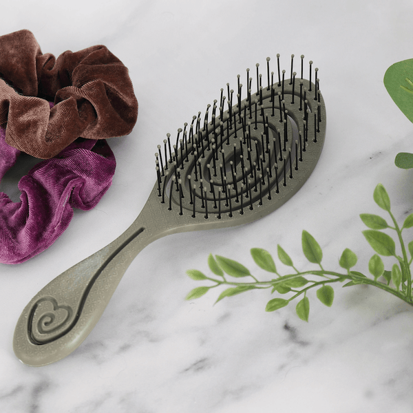 grey brush on marnle style background beside artificial foliage and two neutral colour hair ties