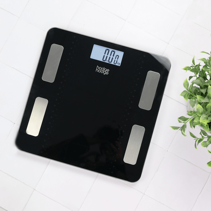 bathroom scale on tiled bathroom floor beside plant displaying 0.00kg on light up LCD screen