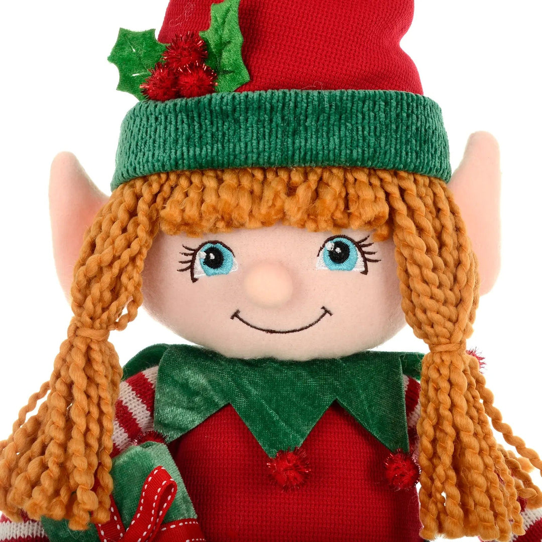 Close up the face of a Christmas Girl Elf figure with glittering holly berry pom poms and ginger hair