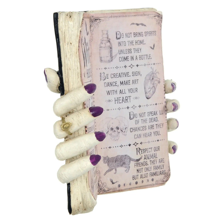 Side view of a Book ornament Halloween decoration with Witch hands and purple nail varnish