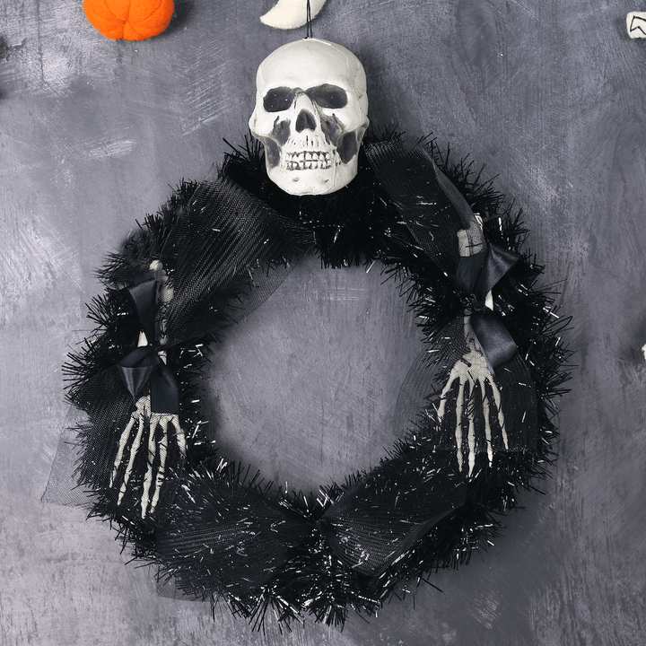 black tinsel wreath with skeleton head and arms on black spooky background with pumpkin garland visible above