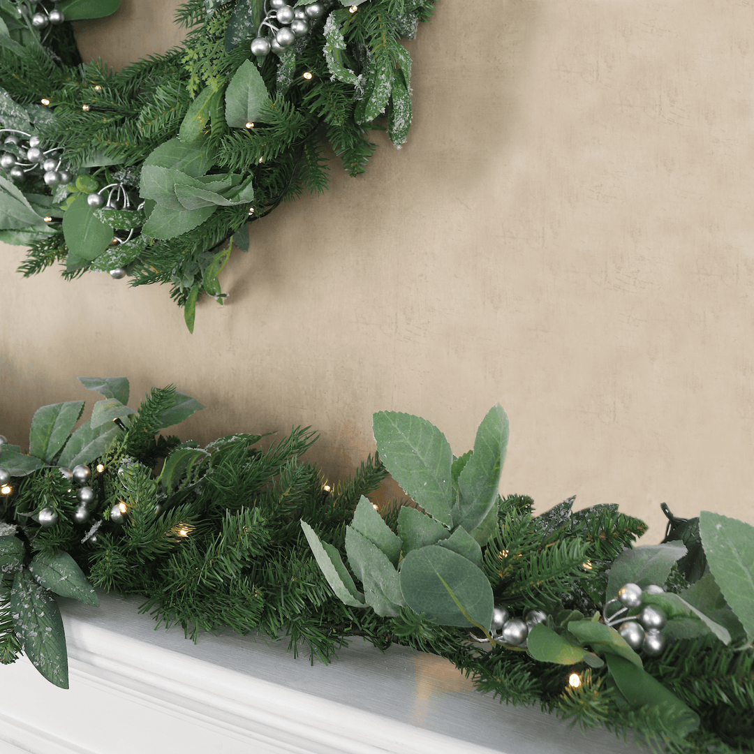 detail shot of matching wreath and garland with warm white led lights hanging on fireplace mantel