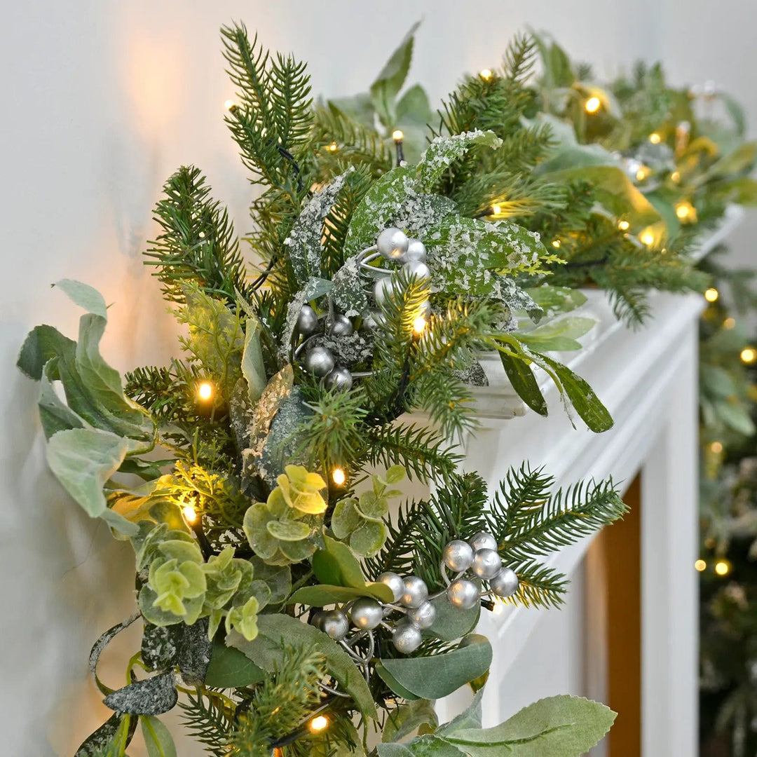 Green Christmas garland with warm white LEDs lights and silver berries draped over a mantlepiece