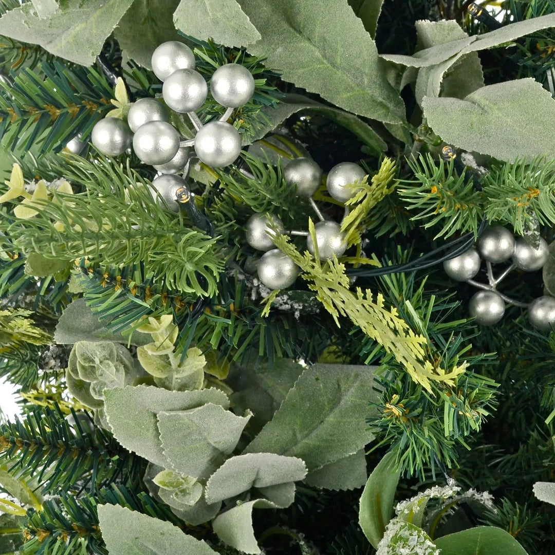 Close up of warm white LED lights, mixed green foliage, frosted leaves and silver berries on a small Christmas tree