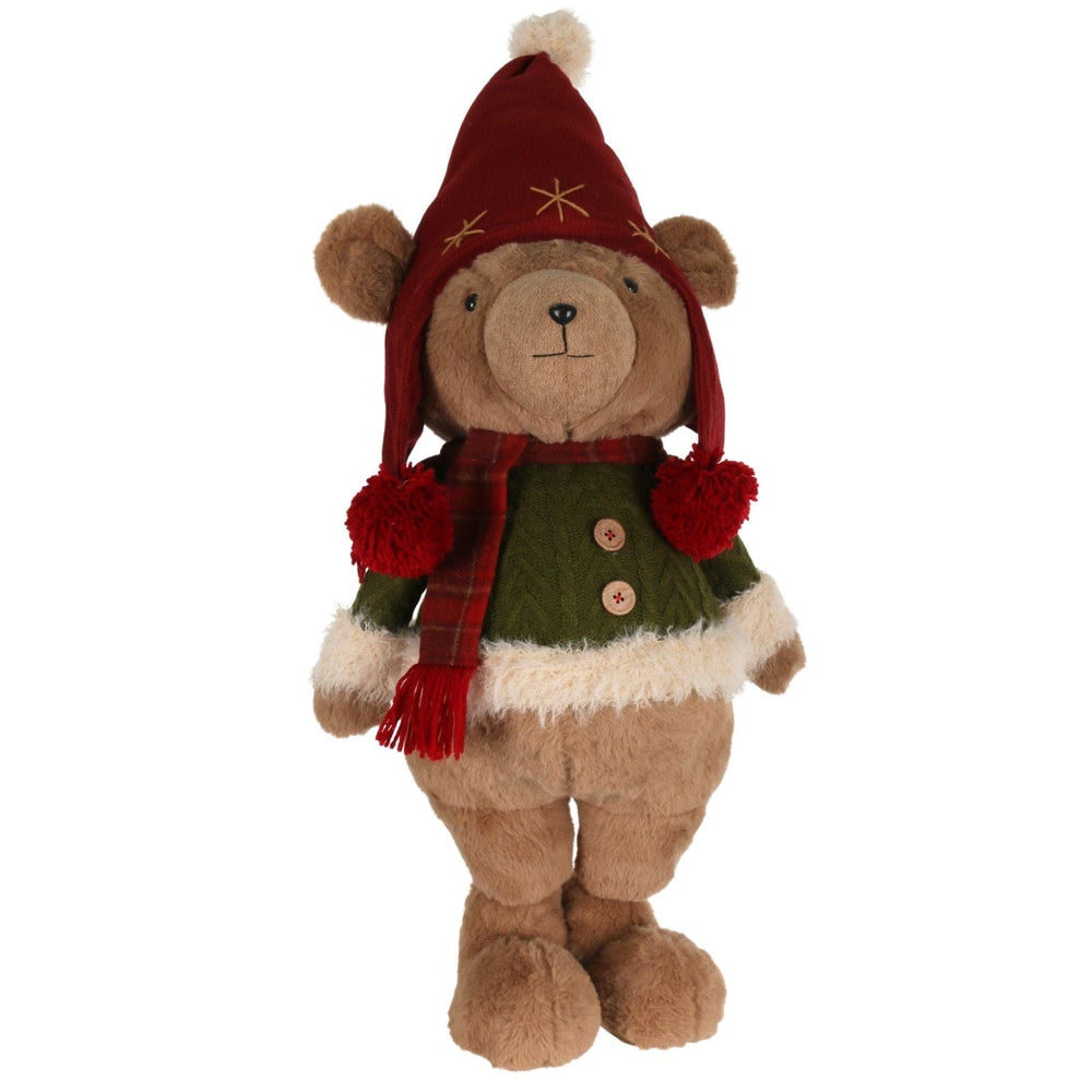 Stuffed teddy bear wearing a festive outfit with a red hat, green sweater, and plaid scarf on a white background.