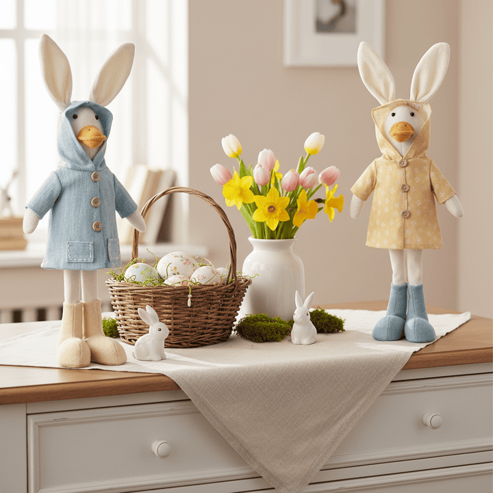 Two stuffed animals in raincoats with a basket of Easter eggs and flowers on a table.