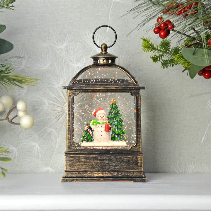 Decorative water glitter lantern with a snowman and Christmas tree inside, surrounded by festive decorations.