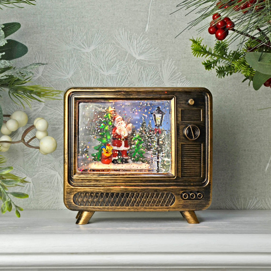 Decorative vintage television with a Christmas Santa glitter water spinner scene inside, surrounded by festive decorations.