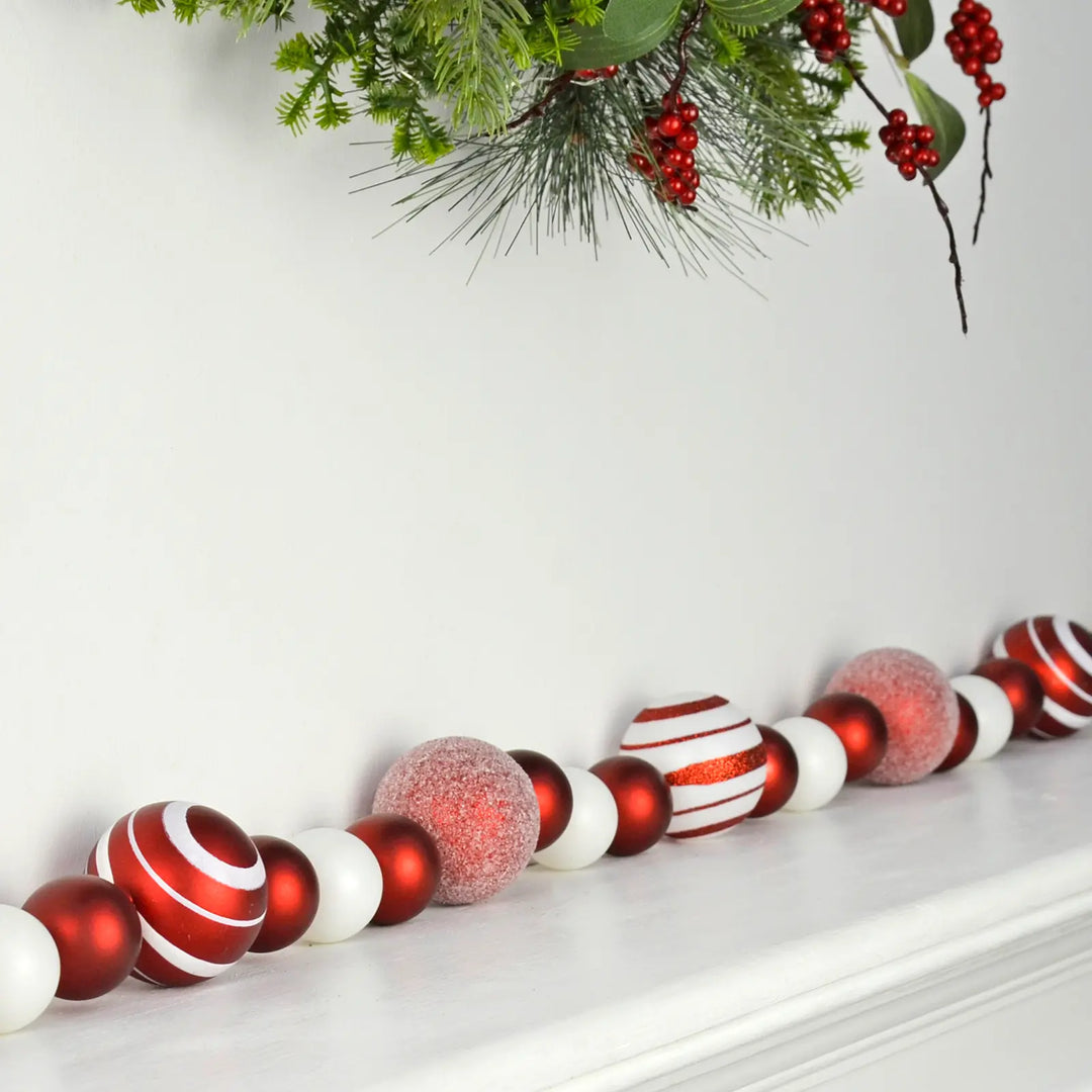 Decorative Christmas garland with assorted size red and white baubles on a fireplace mantel.