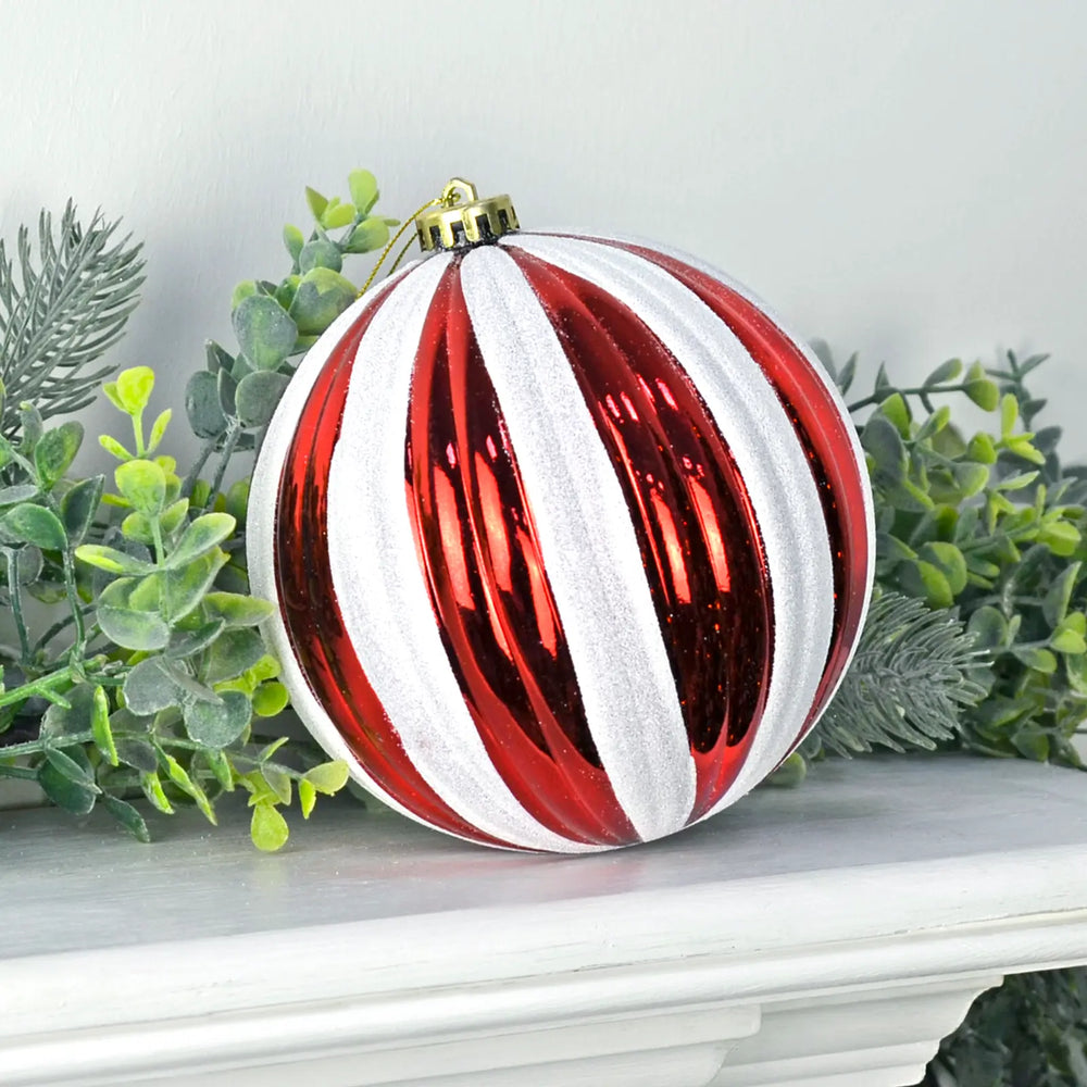 Very large red and white striped Christmas tree bauble on a white mantelpiece with green Christmas garland