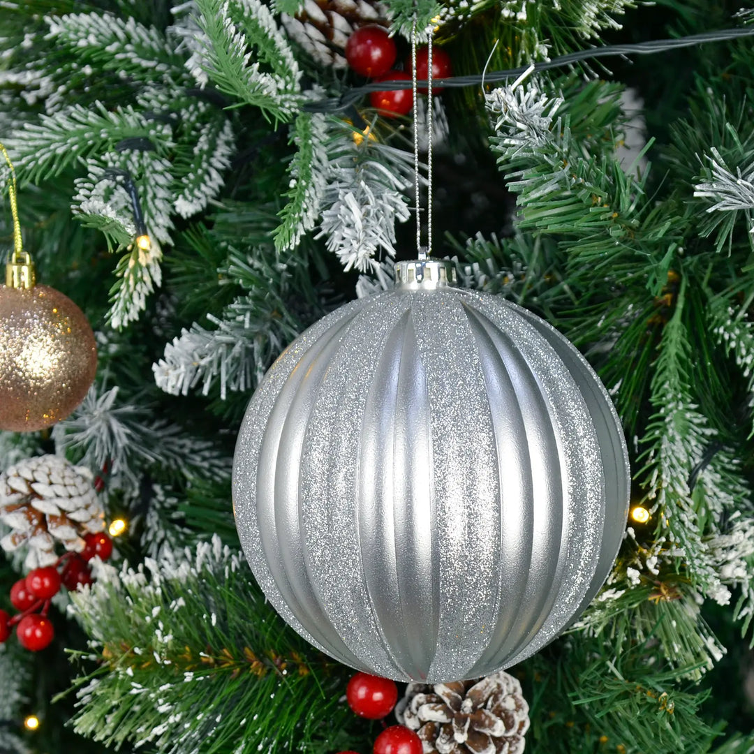Extra large silver glittery Christmas bauble ornament hanging on a decorated tree with red berries and pine cones.