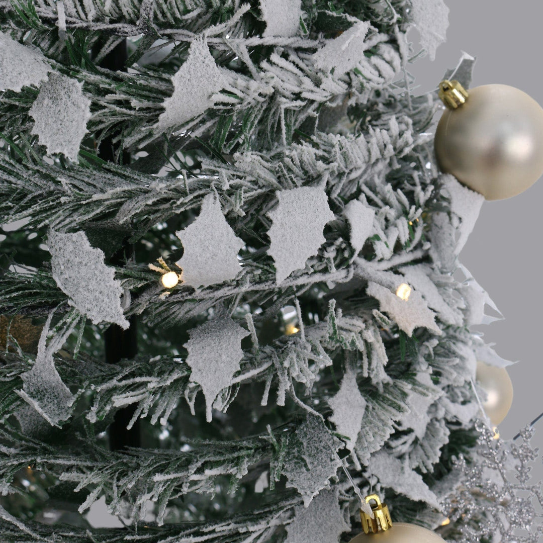 close up of snow flocked holly leaves and branches on white background