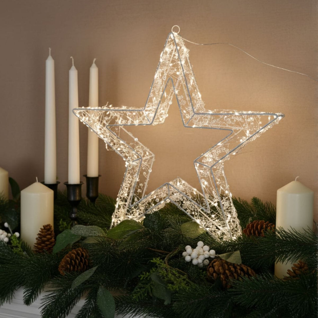 christmas star light on fireplace with candles in background and beige coloured wall