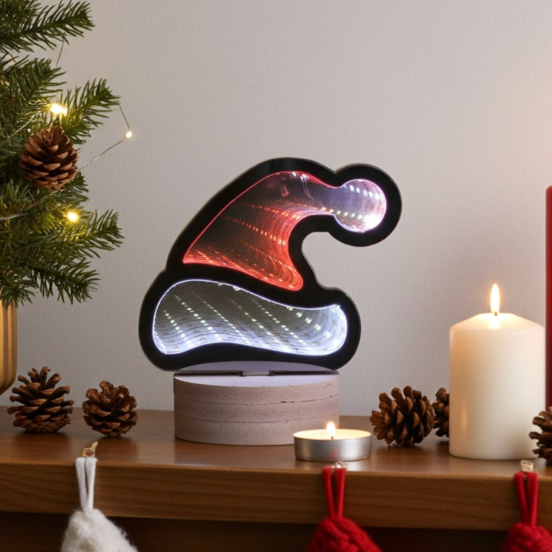 Decorative lamp shaped like a Santa hat on a Christmas-themed shelf with a candle and tree.