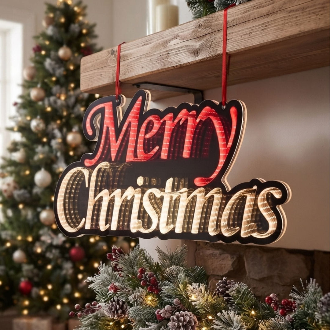 A decorative hanging Christmas sign with red and cream lettering that reads “Merry Christmas,” suspended by red ribbons in front of a fireplace with a decorated tree in the background.